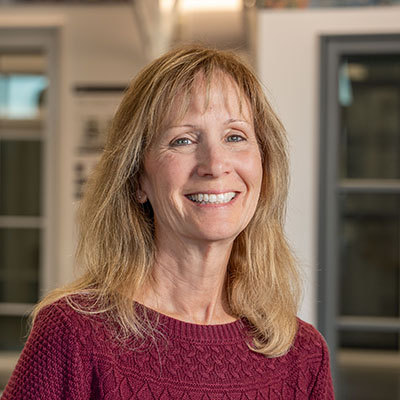A woman with long blonde hair is wearing a dark pink sweater and smiling at the camera.