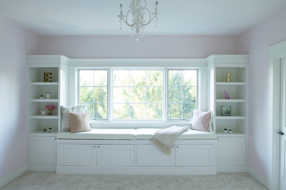 Book cases surround white window seat in pink bedroom