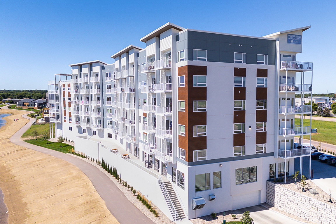 A modern apartment building with large apartment windows and balconies overlooking a waterfront path.