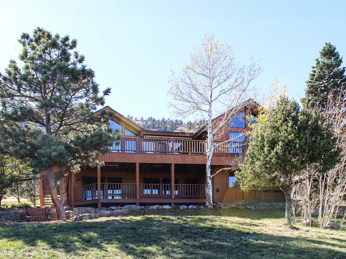 Scenic mountain home featuring wraparound deck, tall windows, and surrounding trees.