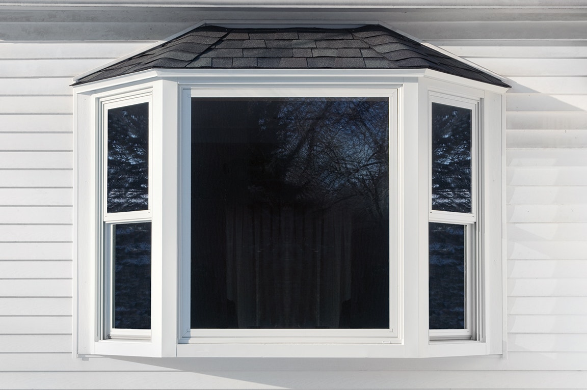A white bay window with a black roof, showcasing a modern design against a light-colored wall.