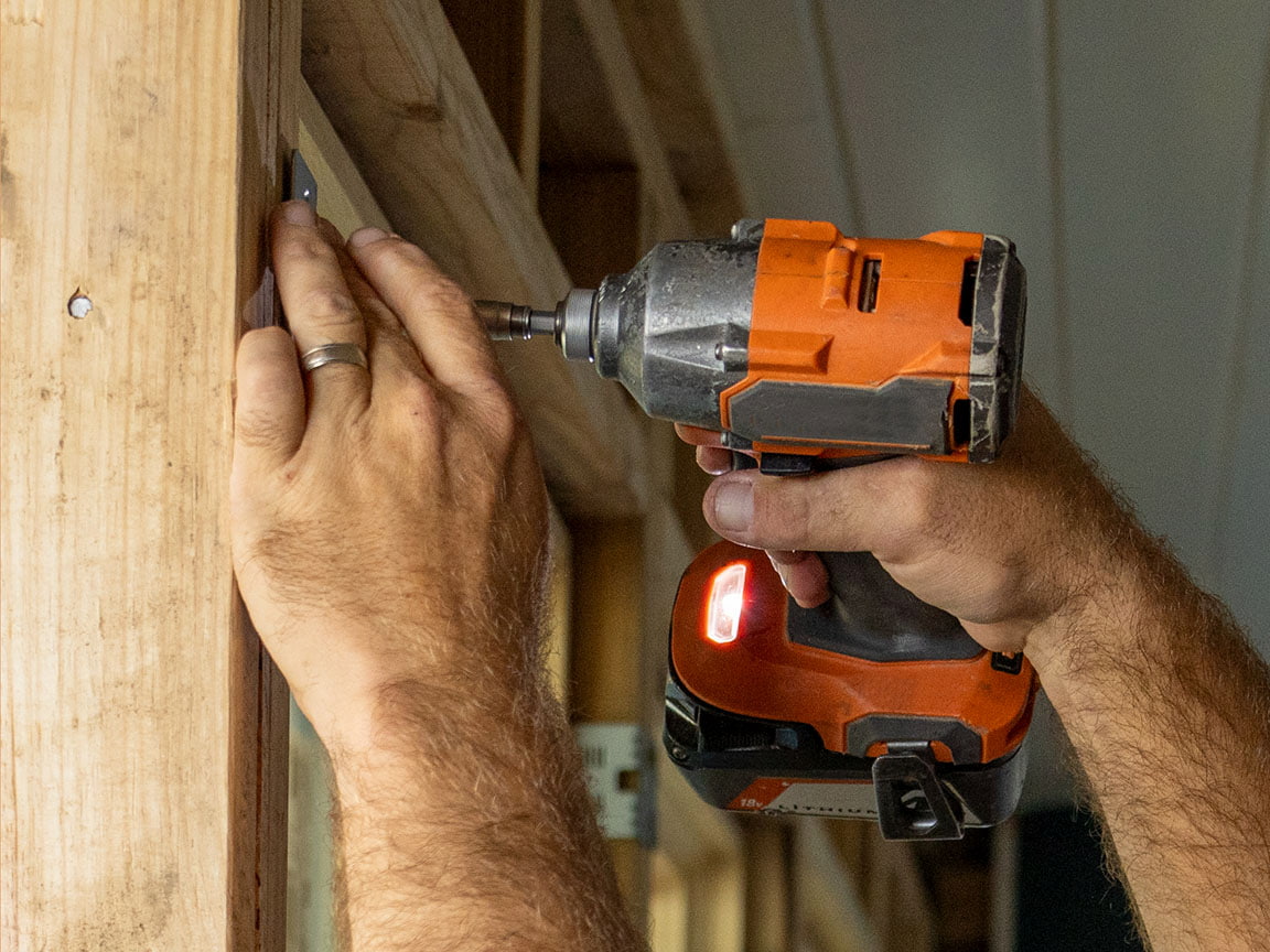 A man is using an orange drill to attach a window to the frame.