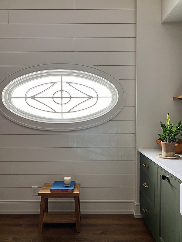 Decorative glass oval window on a paneled wall by a stool with books and a candle