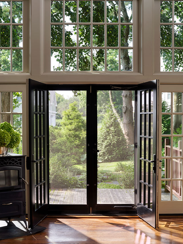 Black patio doors with screens that open to a lush garden view, framed by large windows and wooden flooring. 