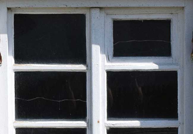 Exterior view of old white windows that have cracked windowpanes.
