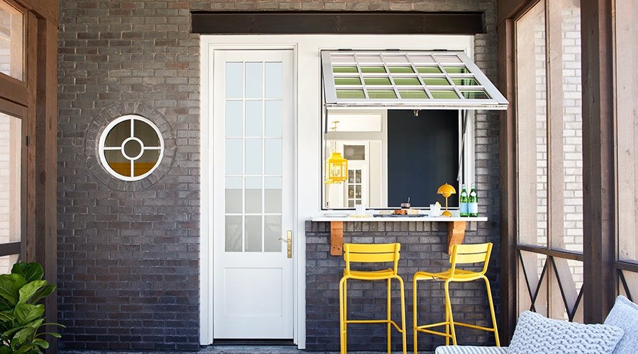 Outdoor patio featuring a circle window, hinged patio door and open window overlooking yellow chairs.