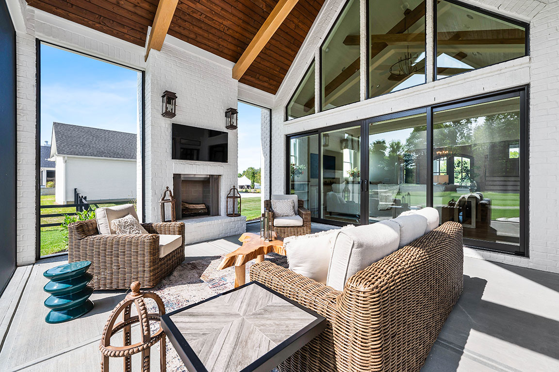 Outdoor covered patio with wicker seating, wood ceiling beams, fireplace, and sliding glass doors 