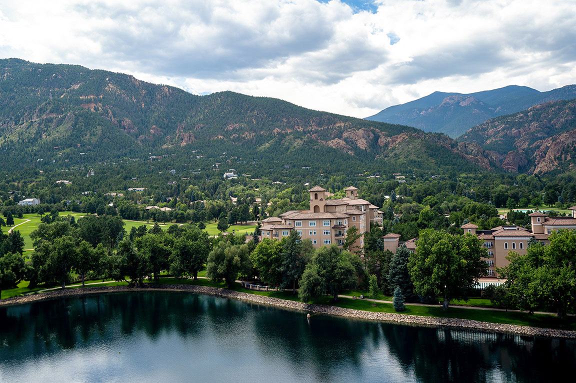 A scenic view of mountains and a lake, showcasing a building with casement windows surrounded by greenery.
