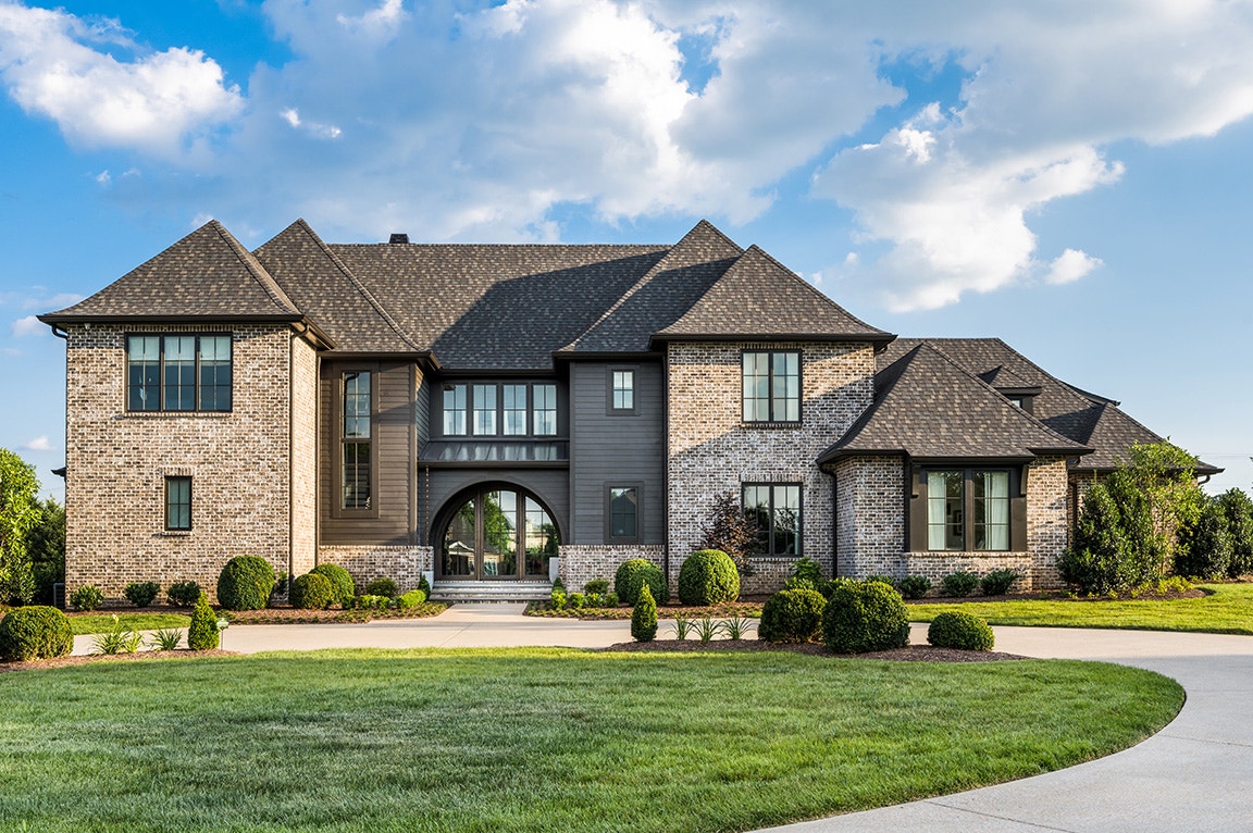 A modern home with a brick exterior and arched windows, surrounded by manicured lawns and shrubs.