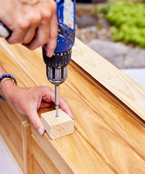 Using a drill to screw a wood spacer to the wood window box