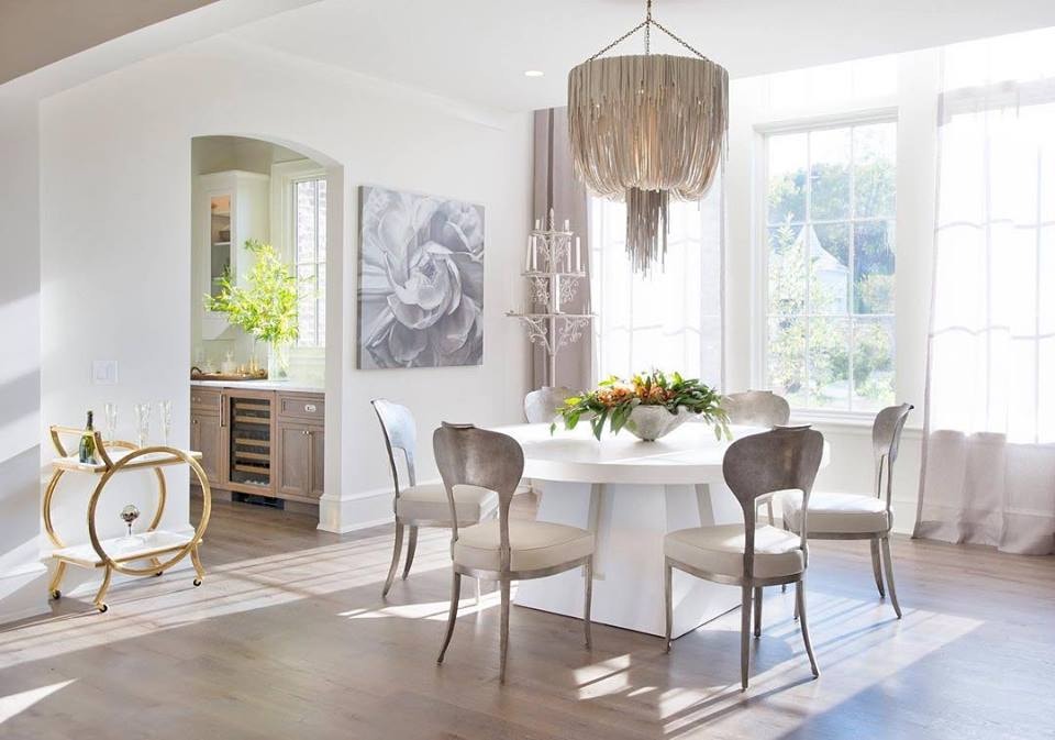 Neutral dining room with white table, wood chairs, beaded chandelier and three tall picture windows light the room