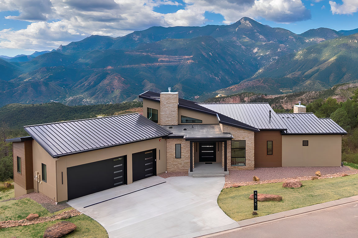 A modern home with black windows and doors, set against a stunning mountain backdrop.