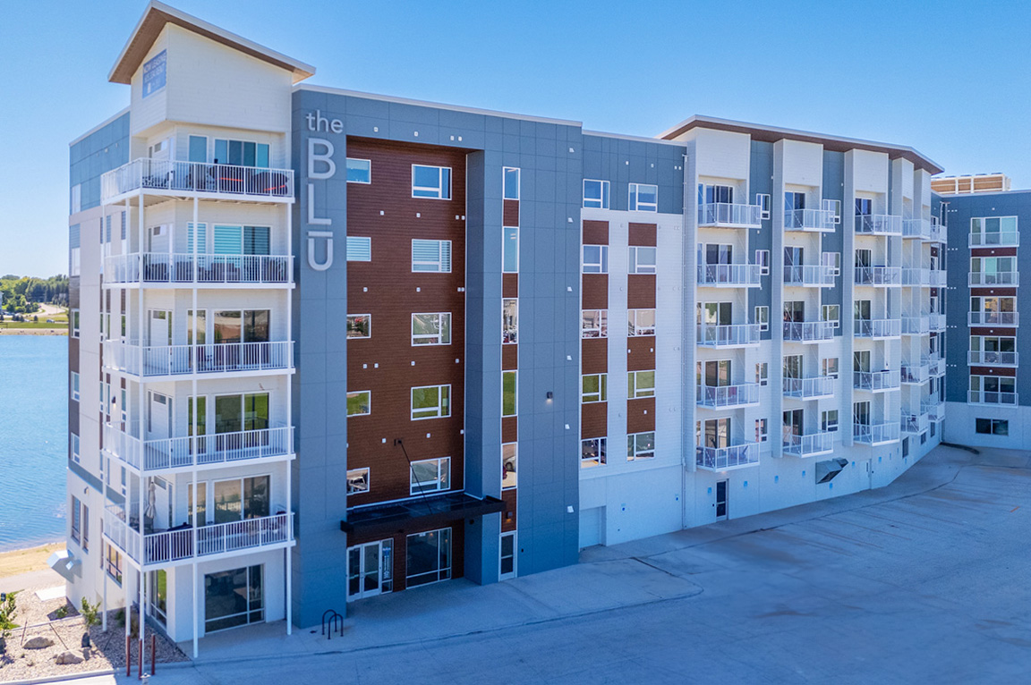 Modern apartment building with large apartment windows and balconies overlooking a waterfront.