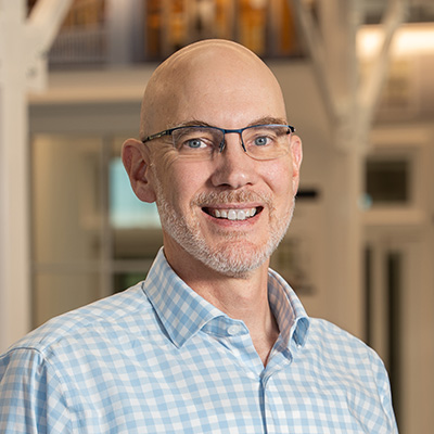 A man with a bald head and a gray beard is wearing a blue and white checked shirt