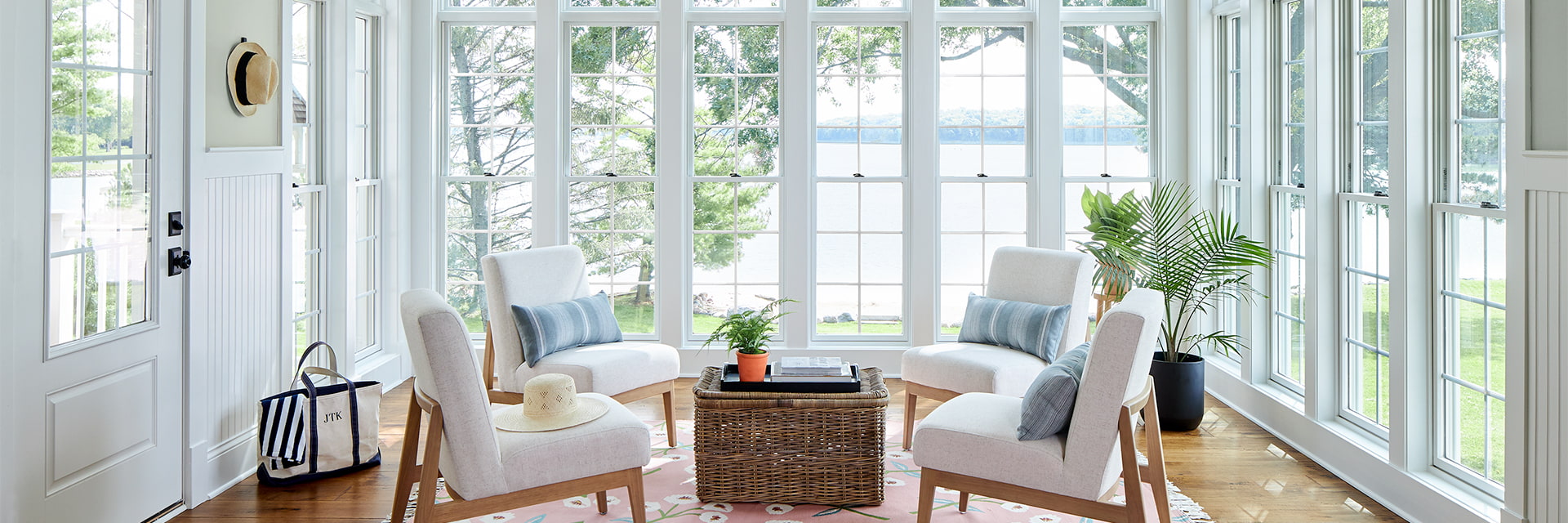 a wall of white double-hung windows open from the sunroom to a lake view outside