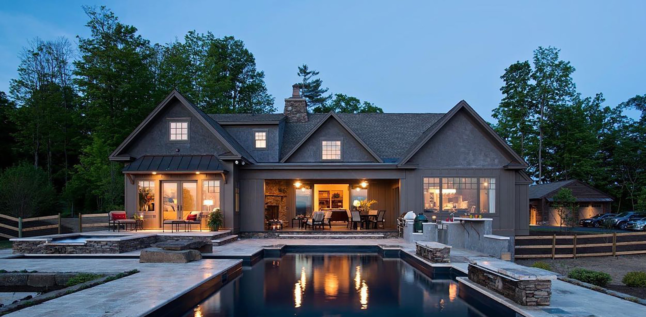 A farmhouse with gray windows and gray patio doors creates inviting exterior space by the pool.