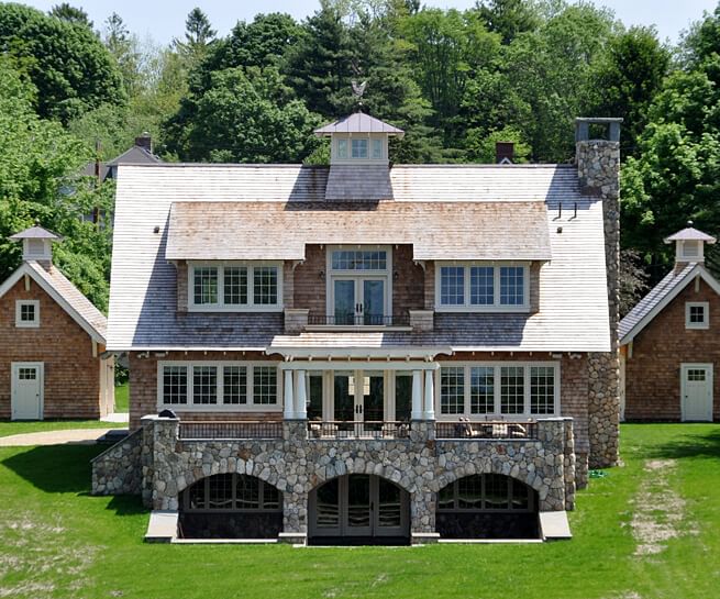 The exterior of a bungalow-inspired shingle-style home features white windows and patio doors.