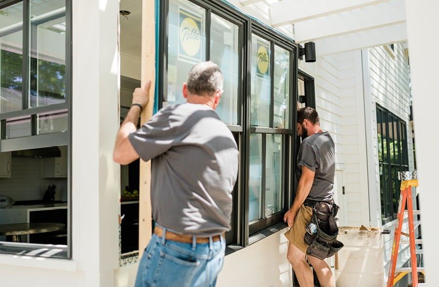 Two Pella employees helping to install a set of black double-hung windows