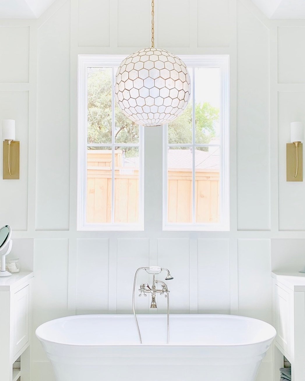 Freestanding bathtub with white picture windows above and a glass pendant light