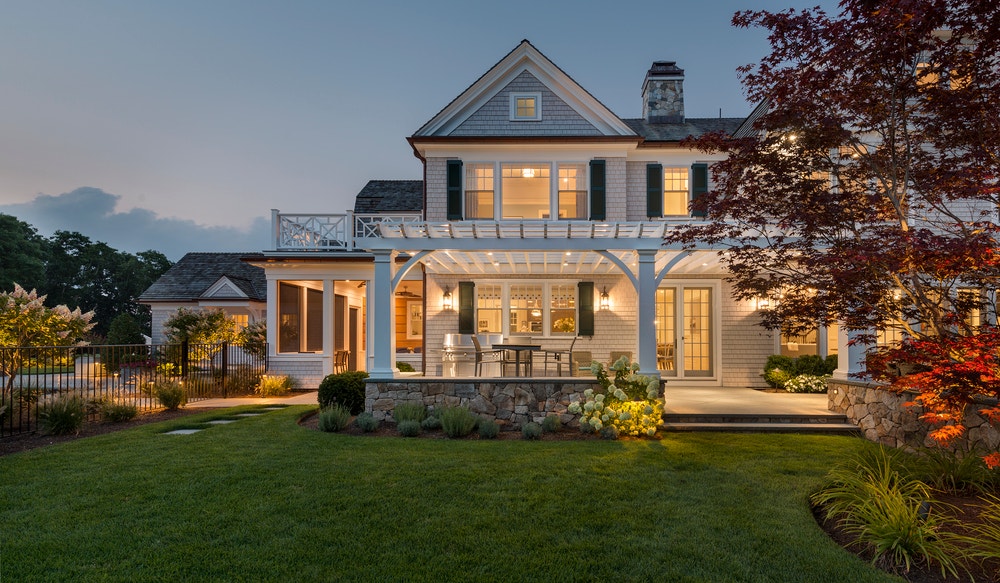 Traditional white two story home as dusk with white wood windows & patio doors