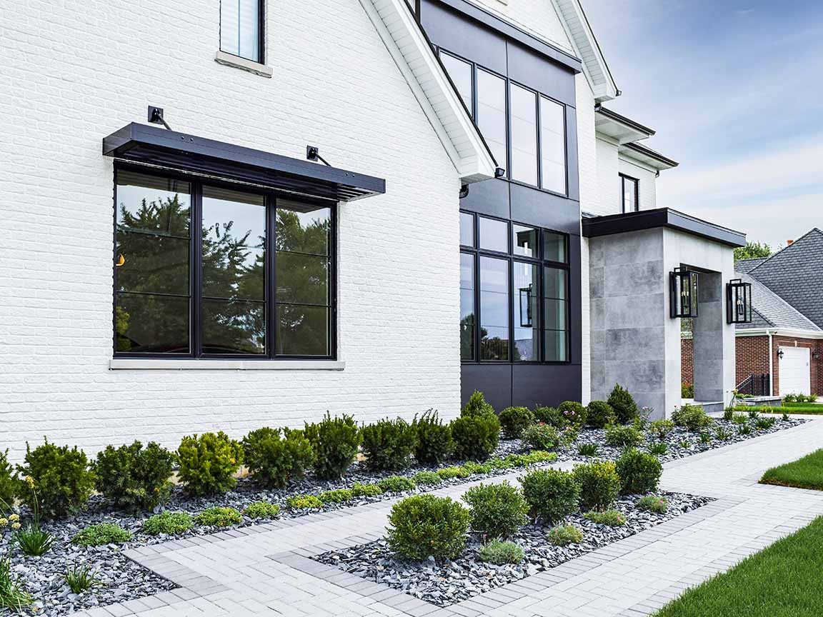 Modern white brick exterior featuring black-framed windows and structured landscaping.
