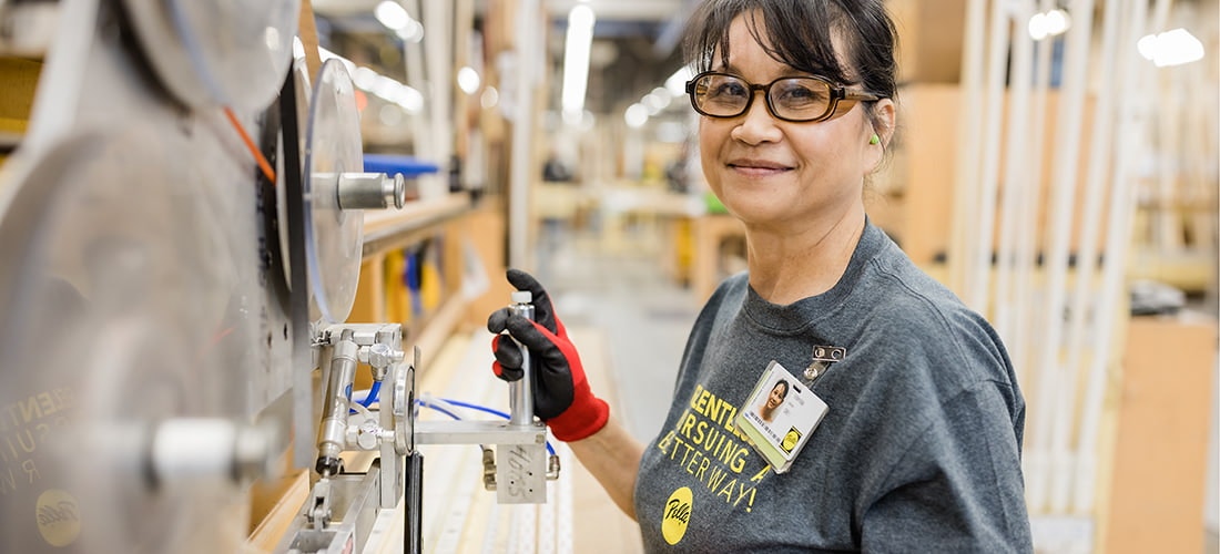 a pella employee pausing to smile at the camera while working on a large piece of glass