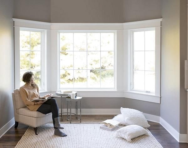 A woman is sitting on a chair in front of a custom set of wood windows to form a bay unit