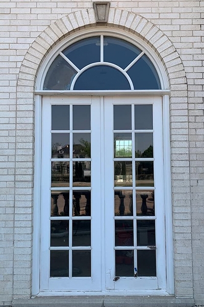 Outdated french doors with arched transom on a white brick home exterior