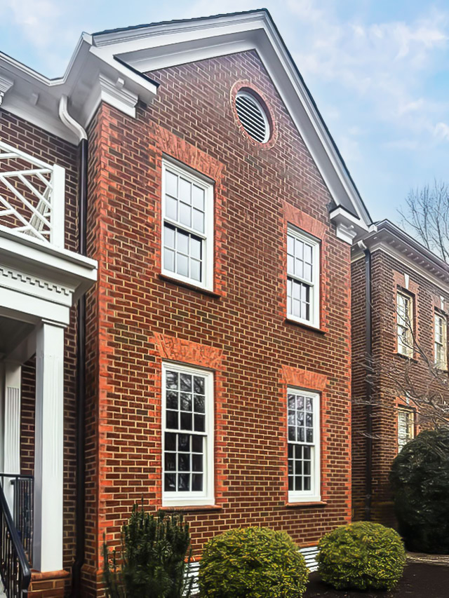 Brick colonial home exterior featuring white double‑hung windows with traditional trim and shutters.