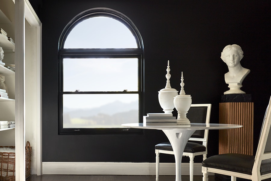 Black double-hung window with transom next to a white bust, bookshelf and table