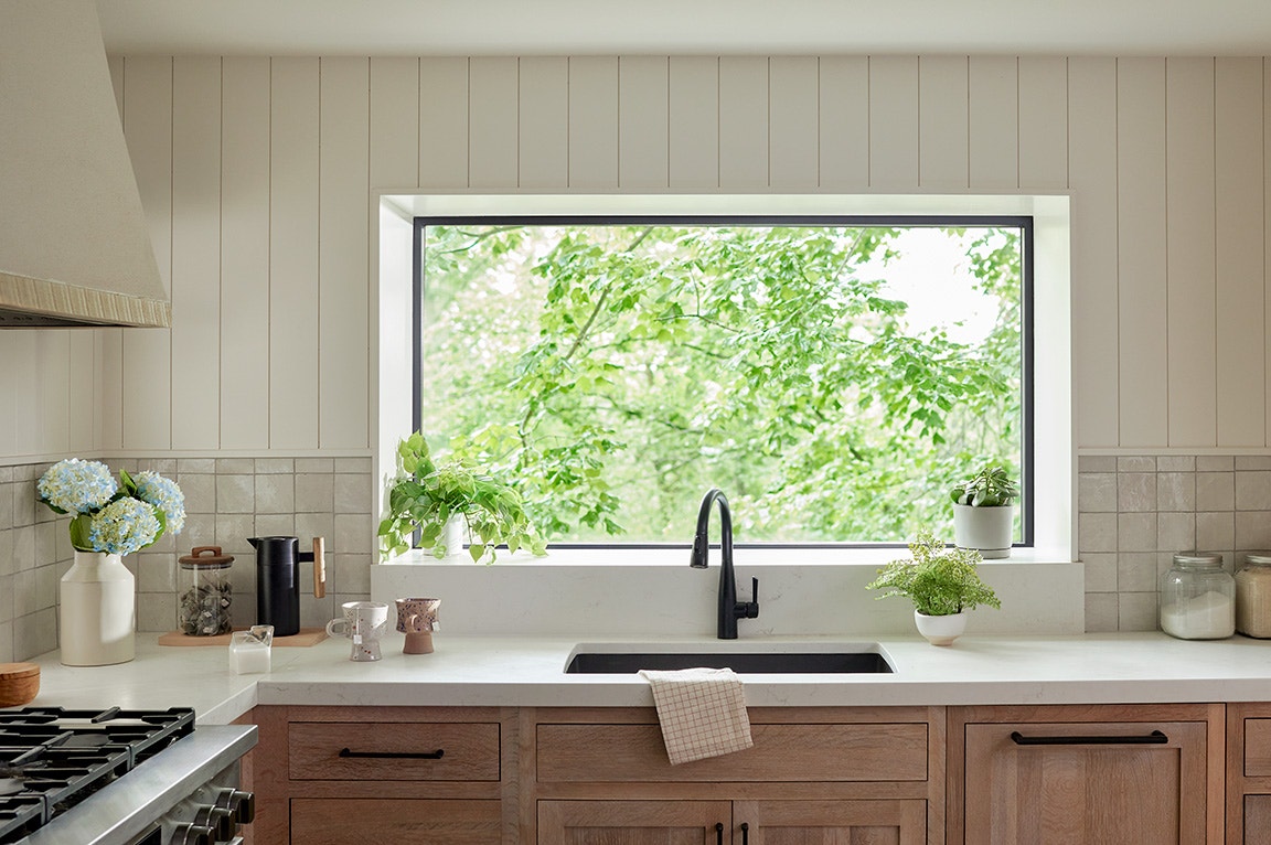 A large black-framed window above a kitchen sink with plants, ideal for choosing best windows for natural light.