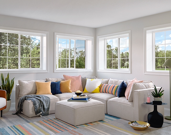 a corner section sofa covered with colorful pillows sits under a series of sliding windows.