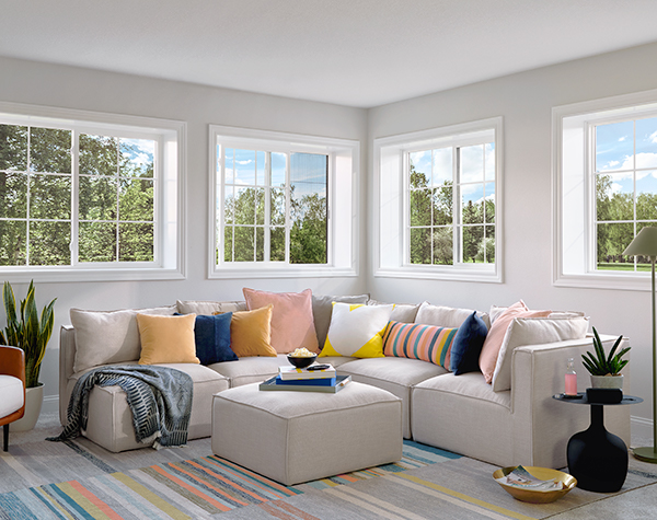 a corner section sofa covered with colorful pillows sits under a series of sliding windows.