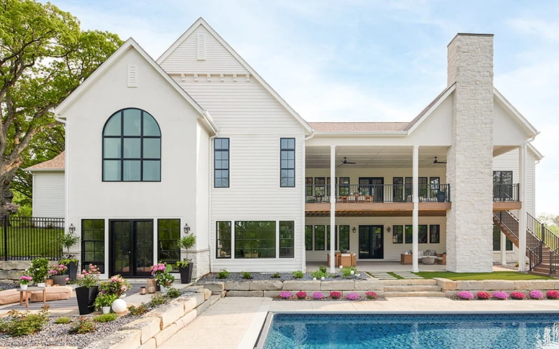 A large two-story white house as seen by the back, revealing a large pool and a two-story deck.
