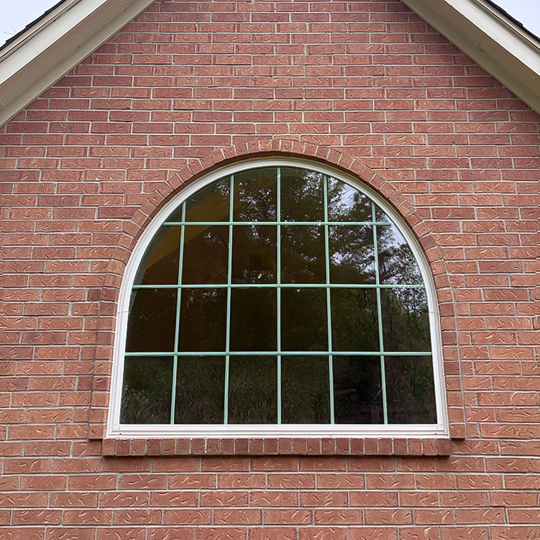 Houston Woodland Home with an arched window set in red brick exterior.