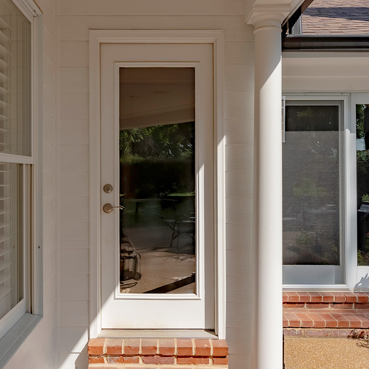 White hinged entry door with full glass panel and silver handle on white siding exterior.