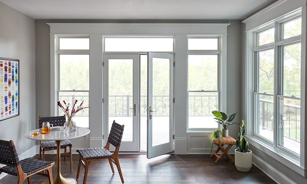A window-walled back sunroom with hinged doors and white double-hung windows, all with white transoms.