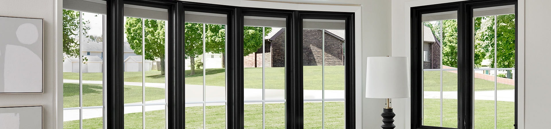 A modern living room featuring a black-framed bow window with a view of green trees and a house.