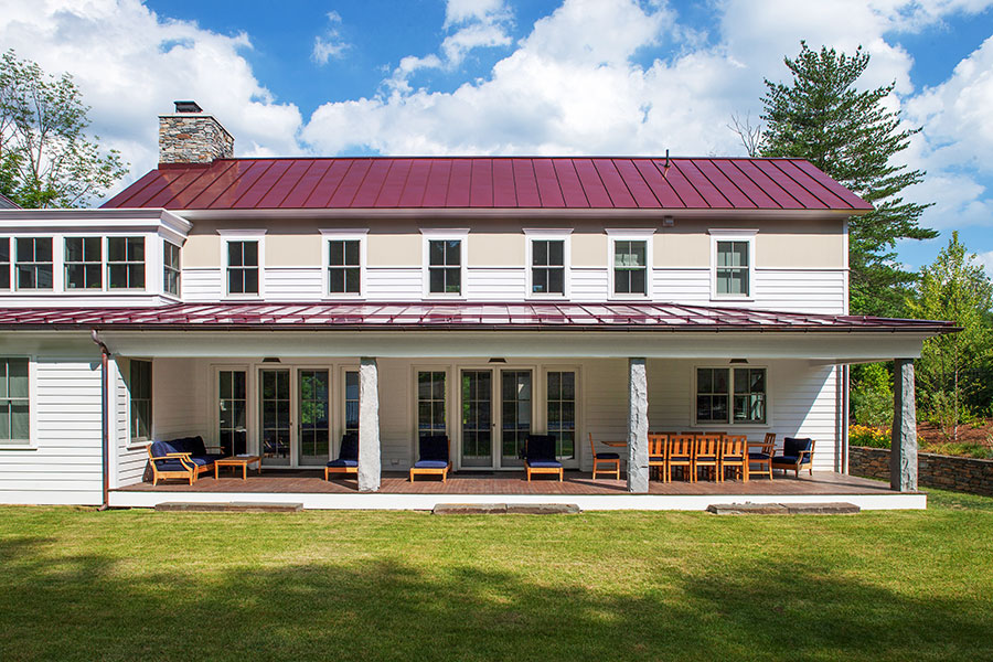 A cottage-style house featuring white windows, with a spacious patio and green lawn.
