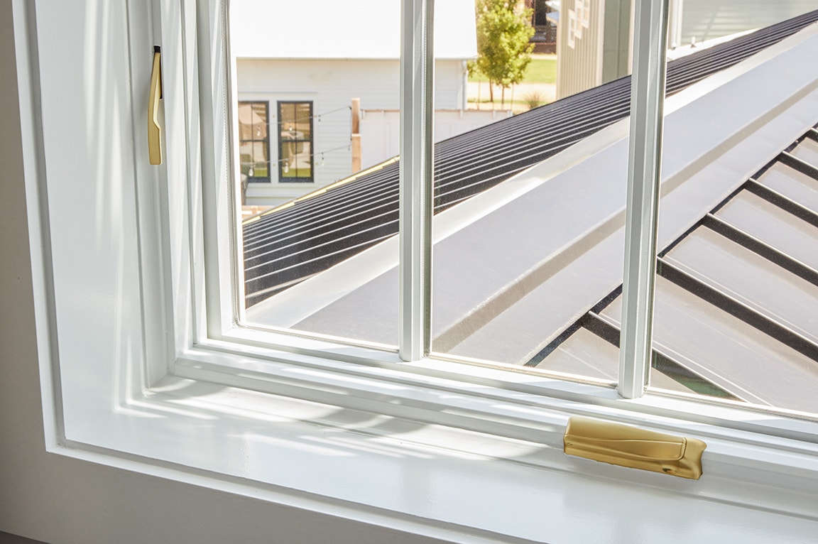 Close-up of interior window trim with a white frame and gold hardware, showcasing natural light.