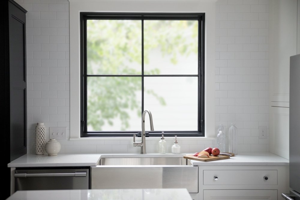 White kitchen counter with farmhouse sink and directly above it is a black square window design