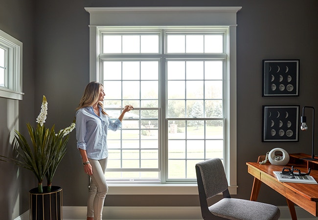 woman standing in home office looking out two large double-hung windows