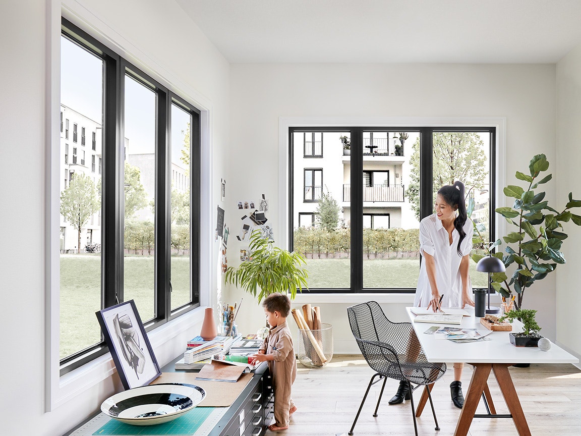 Bright home office with large black-frame windows, plants, and people choosing best windows for the space.