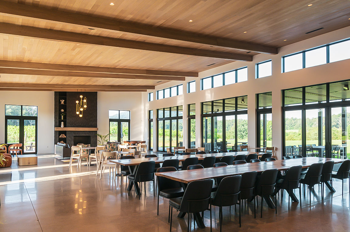 Spacious modern event space with long tables, fireplace, and large windows overlooking vineyard.