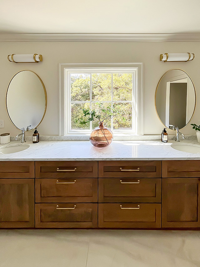 Elegant bathroom with double vanity, marble countertop, wood cabinets, and round mirrors.
