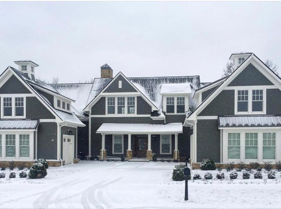Gray farmhouse with white double-hung windows covered in snow