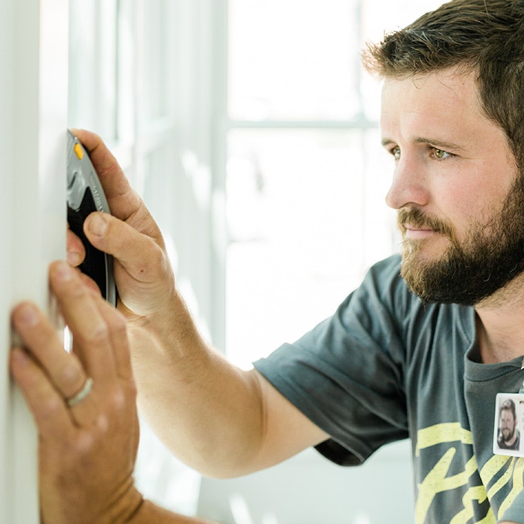 A man measuring a wall for bow windows installation, showcasing precision and craftsmanship.