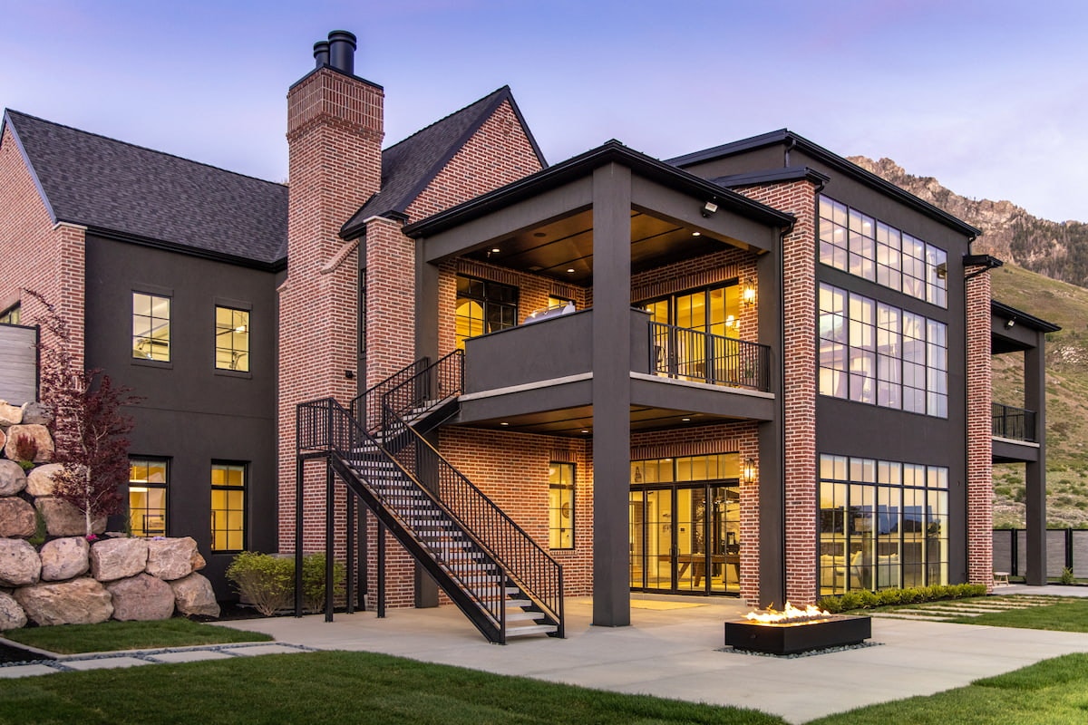 The back of a Utah home's exterior has black windows from top to bottom, and walkout basement doors connecting to the outdoor patio.