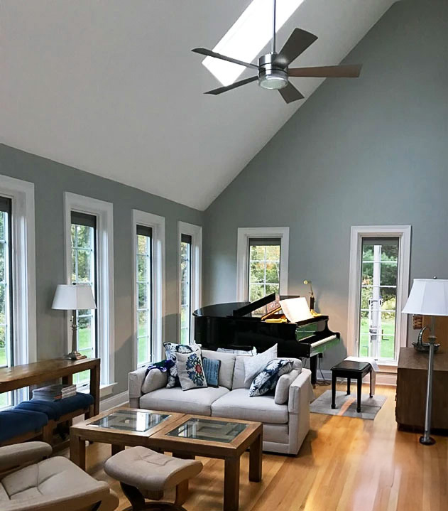 A cozy living room with modern furniture, a piano, and multiple interior white windows allowing natural light.