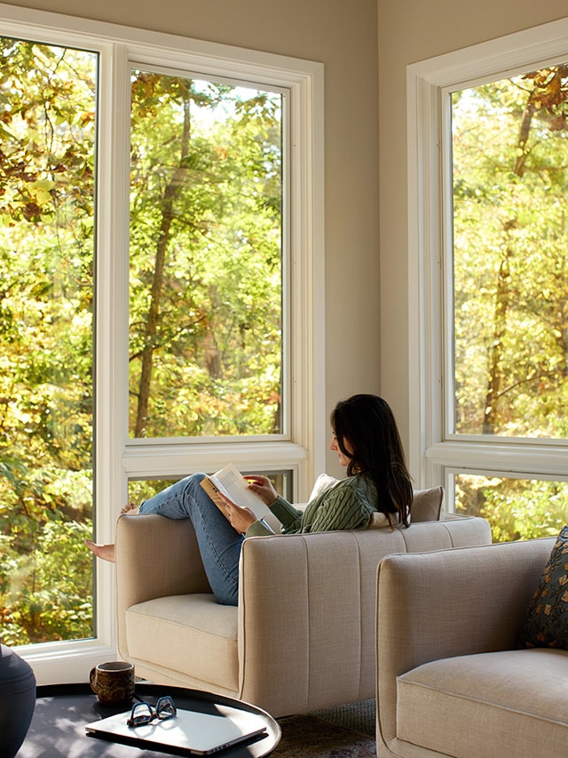 Cozy reading nook with large picture windows overlooking wooded scenery.